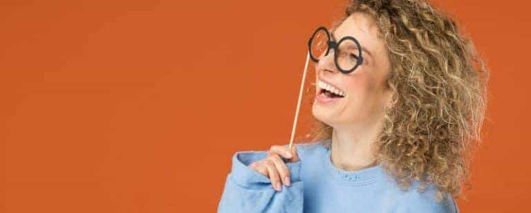 Mujer de pelo rizado ríe mientras juega con unas gafas de cartón ante los ojos