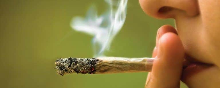 Mano acerca a los labios un porro encendido del que sube humo, en plena calada