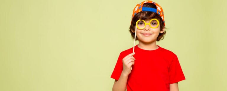 Niño con gorra y camiseta roja juega con unas gafas de broma amarillas