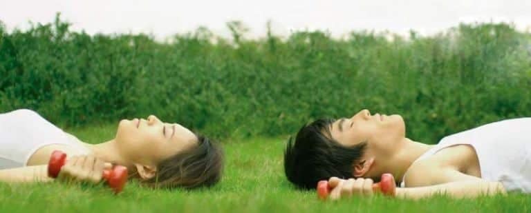 5 razones para iniciar una Terapia de Pareja 9 Pareja tumbada en el césped con mancuernas rojas, descansando tras un esfuerzo compartido