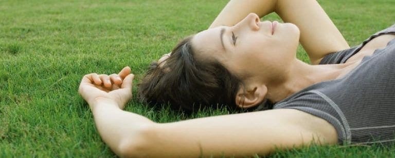 10 maneras de hacer que hoy sea un día inolvidable 6 Mujer tumbada en el césped con los ojos cerrados, disfrutando de un momento de calma