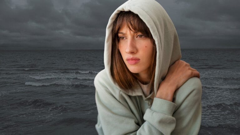 La isla de Alicia: Un relato sobre la salud mental 3 mujer solitaria y triste mira pensativa con un mar de fondo