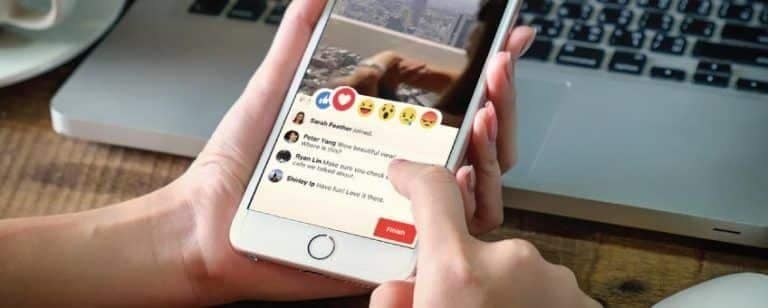 Manos sostienen un móvil con la barra de reacciones y los comentarios de una publicación