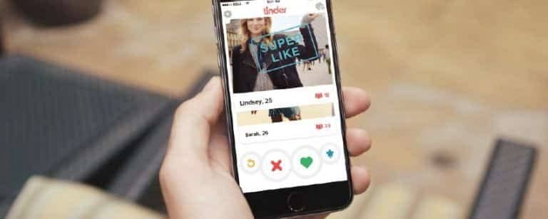 Mano sostiene un móvil con perfiles de Tinder y los botones para descartar o dar like