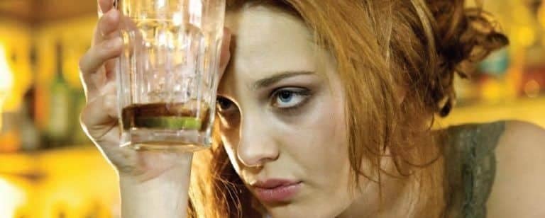 Mujer joven apoya un vaso casi vacío en la frente en un bar, con gesto de abatimiento