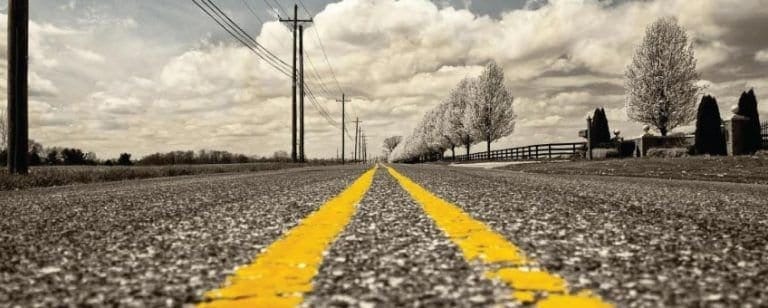 Carretera recta a ras del asfalto con doble línea amarilla perdiéndose en el horizonte, camino por recorrer