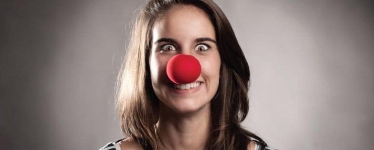 7 pautas fundamentales para mejorar tu estado de ánimo. 4 Mujer con nariz roja de payaso pone una cara exagerada, recurriendo al humor