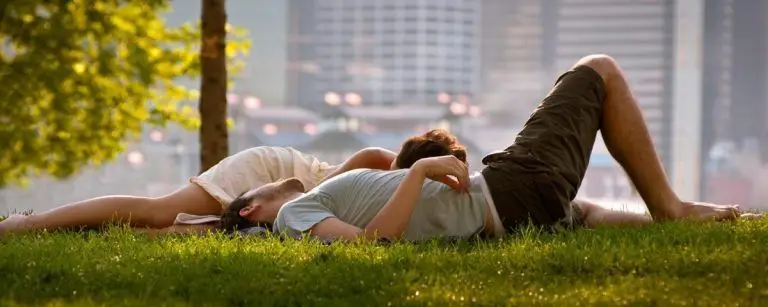 Pareja joven abrazada y tumbada en el césped de un parque, en calma al atardecer