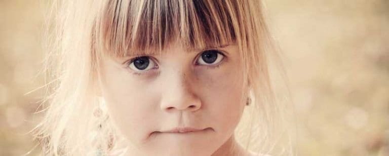TOC en la infancia: "Mi hijo tiene manías" 11 Niña rubia con flequillo mira fijamente a cámara con el labio apretado, en gesto de inquietud
