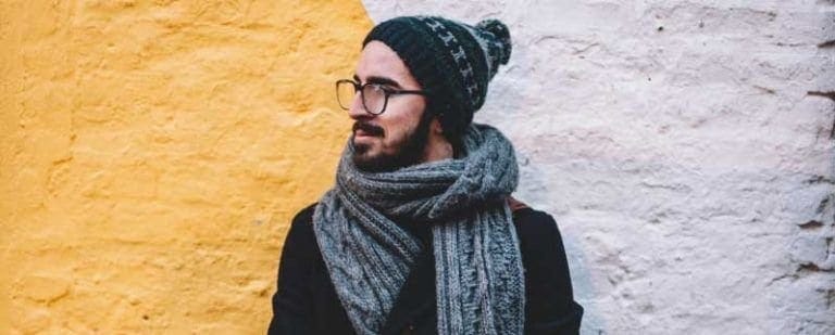 TOC PURO: cuando los pensamientos se apoderan de ti. 4 Hombre con gorro y bufanda de lana mira hacia un lado ante una pared amarilla, ensimismado