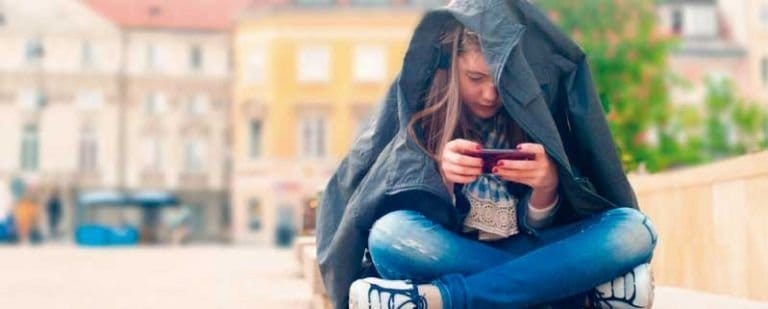 Autolesiones en adolescentes: La búsqueda de alivio a través del dolor. 3 Adolescente se cubre con la chaqueta y mira el móvil sentada sola en una plaza