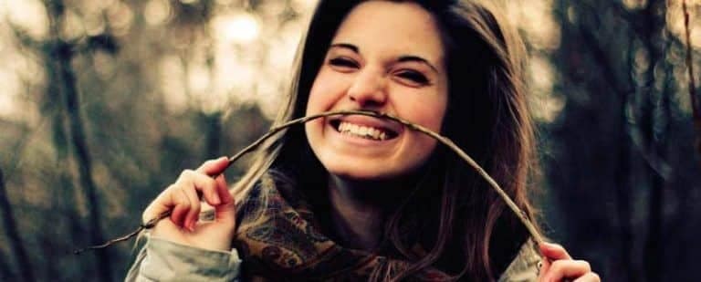 ¿Qué excusa te pones para no ir a terapia? 3 Chica riendo en el bosque mientras muerde una rama fina, con aire despreocupado