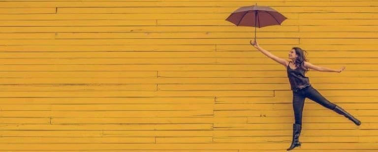 Dependencia emocional: "Sé que tengo que dejarte ir. Pero..no puedo hacerlo". 11 Mujer saltando con un paraguas abierto frente a una pared amarilla, en un gesto de libertad