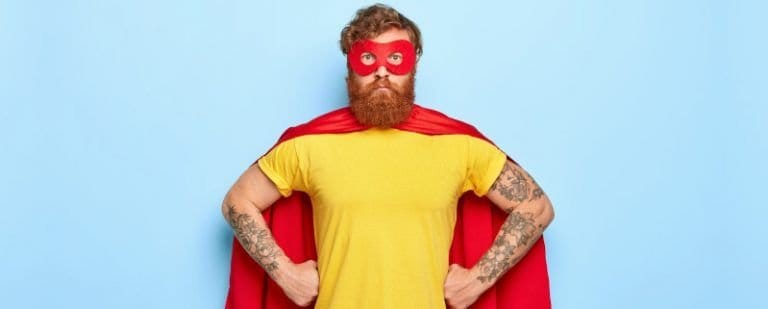 Síndrome del impostor: ¿y si descubren que soy un fraude? 5 Hombre pelirrojo disfrazado de superhéroe posa con los brazos en jarras y expresión poco convencida