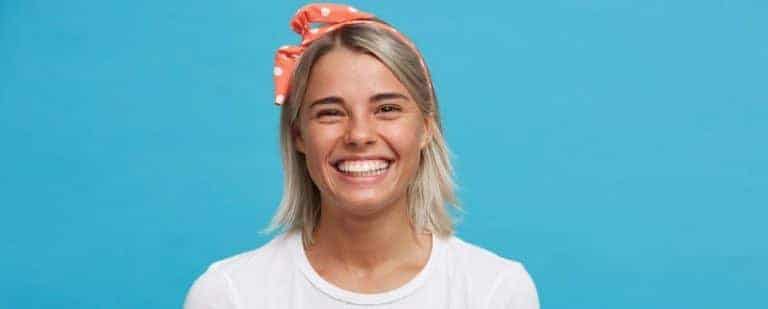 Deseo sexual femenino: ¿por qué no tengo ganas de tener sexo? 1 Mujer con pañuelo naranja de lunares en el pelo ríe con ganas ante un fondo azul