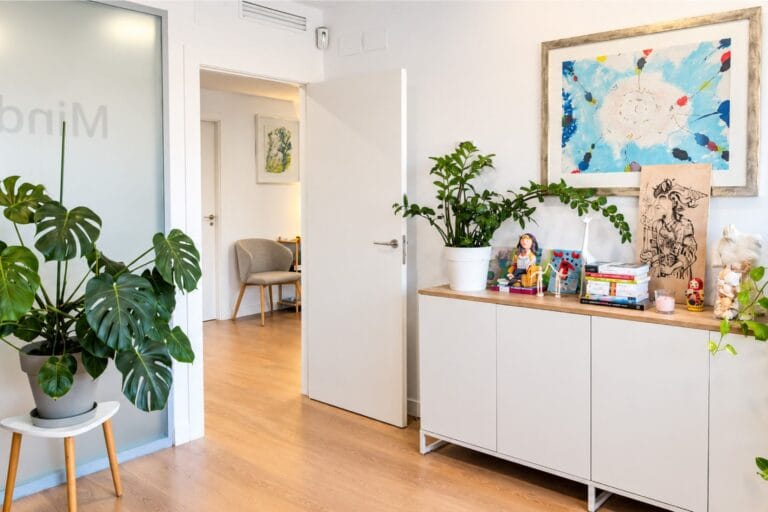 Recibidor de MindUp Psicólogos, con plantas, un aparador con libros y la puerta abierta hacia la sala de espera