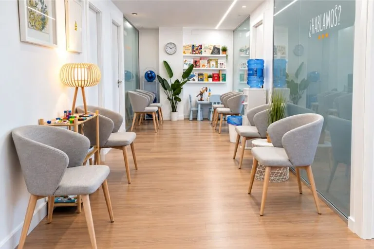 Sala de espera de MindUp Psicólogos en Murcia, con butacas grises, un rincón infantil y el lema «¿Hablamos?» en el cristal